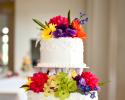 The vibrant wedding flowers compliment the white layers of this traditional wedding cake.