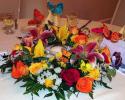 This centerpiece is arranged with bright flowers, lilies, roses, daisies arranged a round a floating candle and fluttering butterflies.