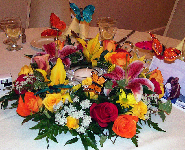 This centerpiece is arranged with bright flowers, lilies, roses, daisies arranged a round a floating candle and fluttering butterflies.