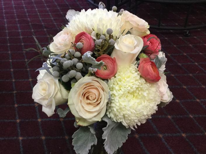 Soft white football mums, peach ranunculus, bruins berries, ivory roses accented with dusty miller.