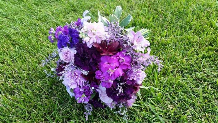 Shades of purple roses, stock and carnations. Bright blue delphinium, limonium and verigated pittsoporum.